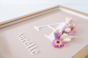 Close up van letterkader met roze en crème kleurige droogbloemen en initiaal en naam uitgesneden in acryl