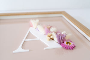 Detail van letterkader met roze en crème kleurige droogbloemen ingekaderd in een houten kader