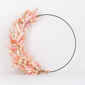 Hangende flowerhoop met droogbloemen in zachte roze en crème kleuren op een zwarte metalen ring