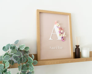 Letterkader met rozige en crème kleurige droogbloemen, een initiaal en naam uitgesneden in acryl op een nude achtergrond op een schilderplank