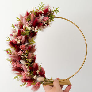 Staande flowerhoop met bordeaux, roze en crèmekleurige droogbloemen op een gouden metalen ring